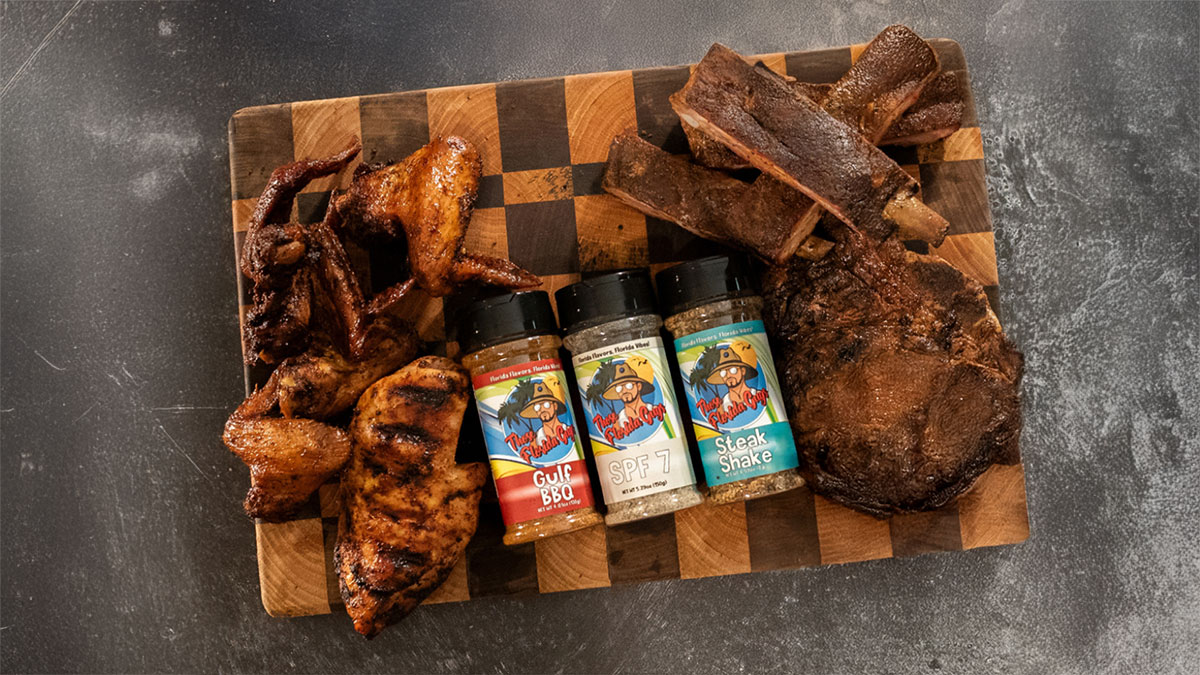 Three of Those Florida Guys BBQ rubs on top of a cutting board surrounded by pieces of meat